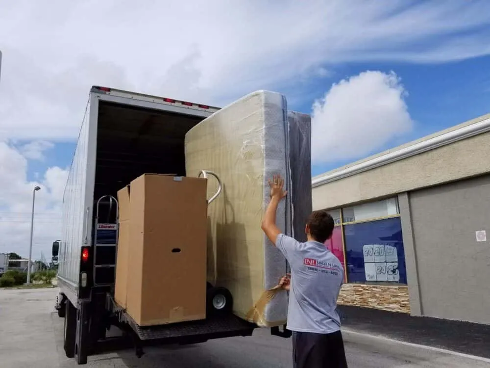 Mover in LNL branded t-shirt loading a wrapped mattress onto a box truck