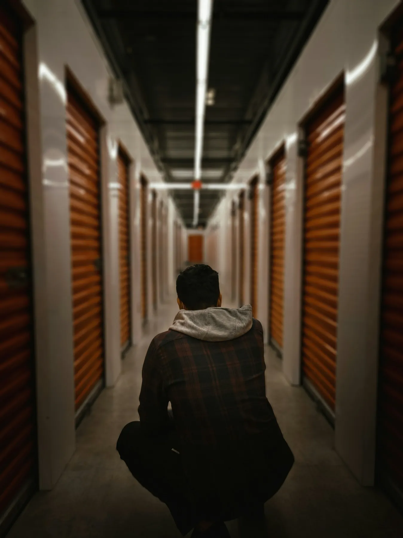 Man crouching in a self-storage hallway lined with orange roll-up doors